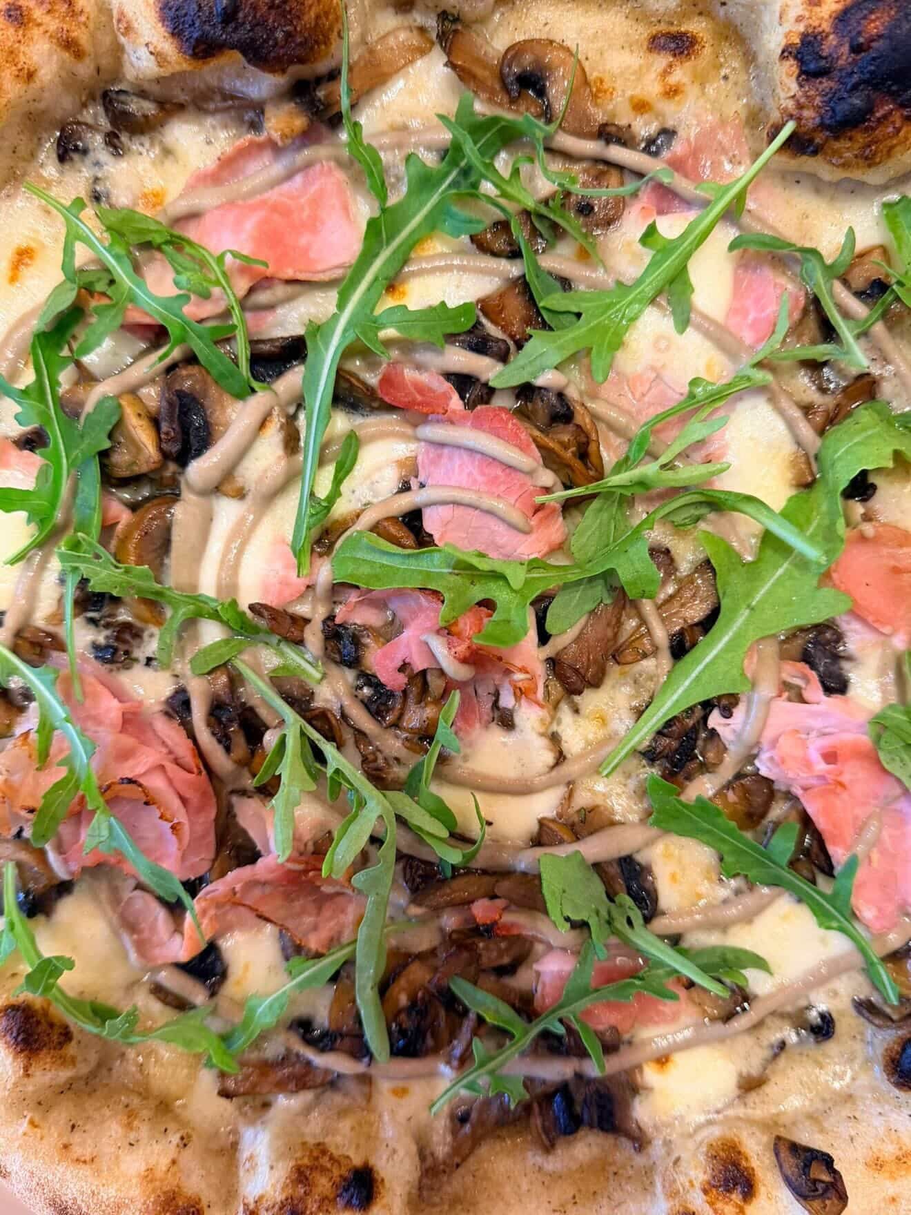 A pizza with arugula and cured meat at Pizzaclub